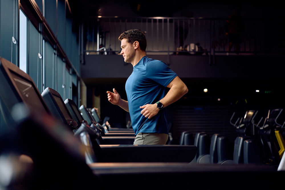 Mid adult sportsman running on treadmill at health club