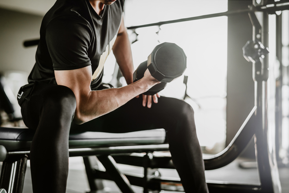 Cropped shot of fitness man doing concentration curls exercise working out with dumbbell in gym. Weight training concept