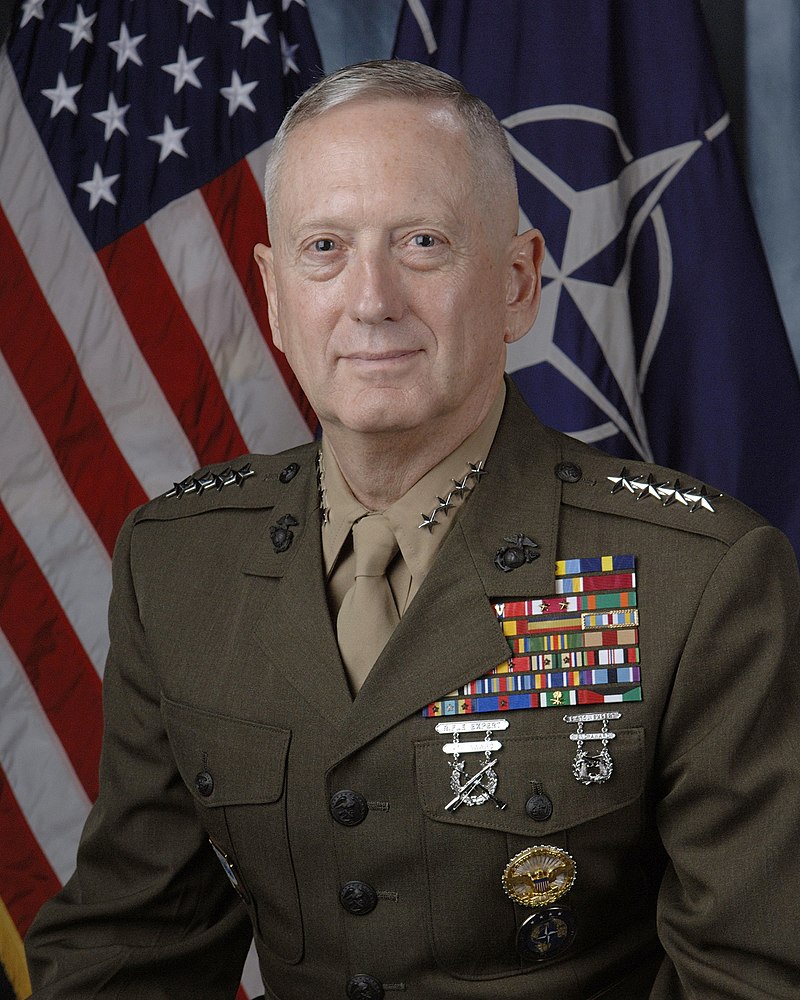 US Secretary of Defense, James Mattis in Military Uniform. Behind him is a large collection of books on a bookshelf.