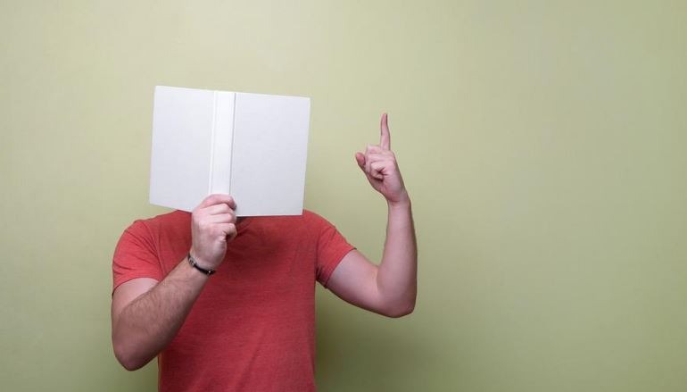 A guy reading a book while signaling up using his hands