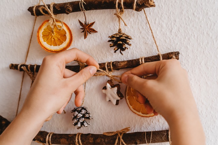Woman hands decorating handmade craft Christmas tree made from sticks and natural materials hanging on wall. Sustainable Christmas, zero waste, plastic free, eco friendly.