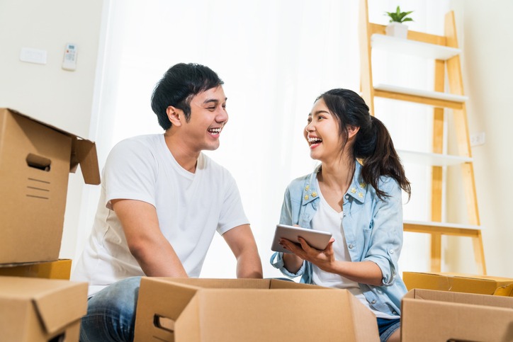 Happy young Asian couple moving in to new house, using digital tablet organizing things and unpacking boxes together. Home relocation, domestic lifestyle, or love relationship concept